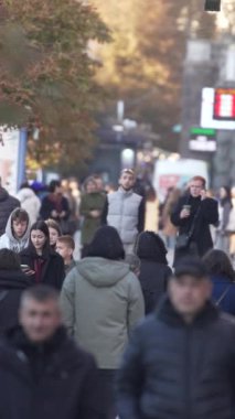 KYIV, UKRAINE - 6 Ekim 2024: Sonbaharda sokakta yürüyen insanların dikey videosu, yavaş çekim