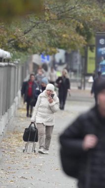 KYIV, UKRAINE - 6 Ekim 2024: Sonbaharda insanlarla dolu bir şehir sokağının dikey videosu, yavaş çekim