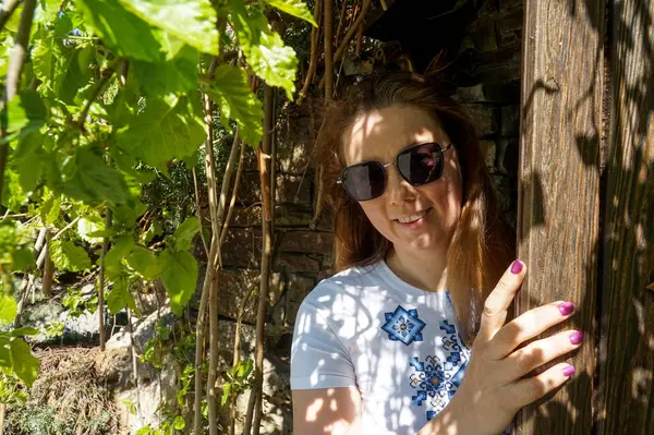 Nakışlı elbiseli bir kız kapının arkasından dışarı bakar.                         