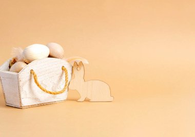 Paskalya ahşap yumurtaları ve bej arka planda ahşap dekoratif tavşan. Boş tebrik kartı. Doğallık, ekoloji, mevsimlik, bahar, tatil kavramı. Boşluğu kopyala, yakın plan.