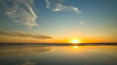 Düz bir kumsalda, ılık sarı parlak güneş batıyor..