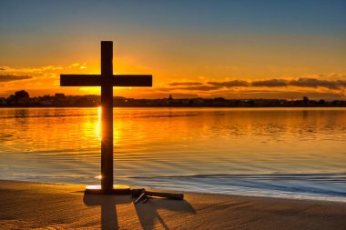 Çekiç ve üç çivi, ahşap bir haçın yanında, şafak vakti harika bir gökyüzü, bir su koyunun üzerinde..