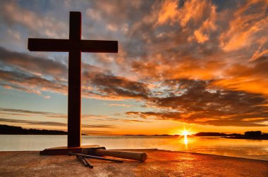 Tahta haç, çekiç ve çarmıhın ucunda üç büyük çivi. Su koyunun üzerinde harika bir günbatımı.