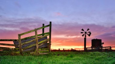 Çiftlik rüzgar pompası yanında su kulesiyle biraz yıpranmış görünüyor. Arka planda harika bir gündoğumu gökyüzü var..