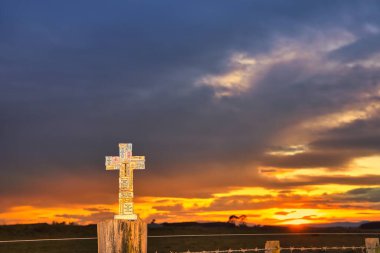 Her blokta cesaretlendirici sözler yazan harika bir taş haç. Çitin üzerinde otururken, arka planda harika bir gün doğumu gökyüzü var..