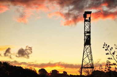 Sunset behind steel frame viewing tower. The sky has storm clouds that are lit up by the setting sun.