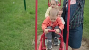 Güzel okul öncesi çocuklar ve genç anneler parkta salıncakta gülüyorlar. Küçük bebek gülüyor, Tahterevalli tahtasında sallanarak eğleniyor. Mutlu çocukluk kavramı, olumlu duygular, POV.