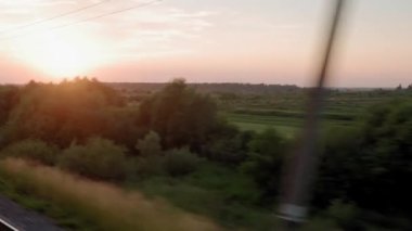 Yüksek hızlı trenin penceresinden manzarası güzel doğa manzarası vahşi arazi ve orman akşam bulutlu gökyüzü günbatımı yaz arkaplanında. Ulaşım, seyahat, demiryolu, iletişim konsepti.