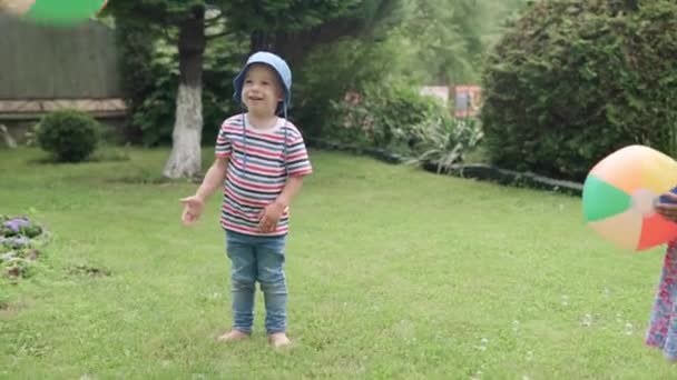 マルチカラービーチボールで走る幸せな子供たち 男の子と女の子の娘と息子は 晴れた夏の日にイディリック郊外の家の裏庭の芝生でゲームを楽しむことができます 幼少期の家族の概念 — ストック動画