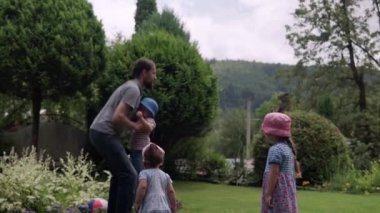 Happy Family Funny Young Dad with Beard Throws the Kids Up High by Arms. Father, Preschool Daughter and Son Have Fun Playing Games in the Backyard Lawn of Idyllic Suburban House on Sunny Summer Day