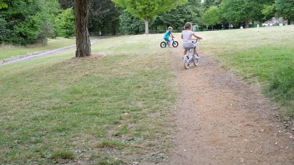 子供のためのスポーツ活動 夏の干ばつ乾燥した草の中で公園の道を自転車やスクーターに乗って遊んでいる小さな子供たち 弟と妹は一緒に遊んでいます 子供の発達の概念 — ストック写真