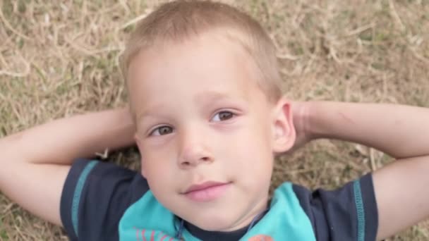 Mały Szczęśliwy Poważny Przemyślany Chłopiec Leżący Żółtym Trawniku Suche Trawy — Wideo stockowe