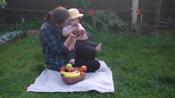 Szczęśliwa Młoda Radosna Matka Trzymająca Dziecko Jedzące Owoce Zielonej Trawie — Wideo stockowe