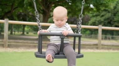 Komik, küçük, tombul kız, ablası, yeni doğmuş erkek kardeşi salıncakta sallıyor. Bebek oyun parkında oynuyor. Çocuk Eğlencesi, Çocukluk, Çocuk Geliştirme, Mutlu Aile Kavramı.