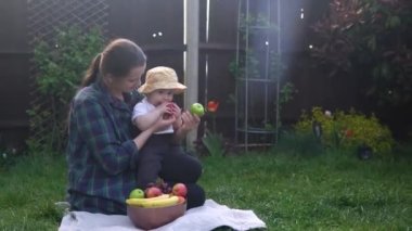 Mutlu Genç Neşeli Anne Yeşil Çimlerde Bebek Yiyen Meyveler Tutuyor. Sevimli Anne Bebek Arka Bahçe Bahçesinde Dışarıda Sevgiyle Oynuyor. Ailesi olan küçük çocuk. Aile, Doğa, Ekoloji Kavramı