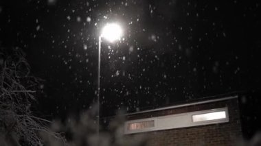 Birleşik Krallık 'taki ilk kar yağışı örtüsü kara arka planda. Gece Yolu 'ndaki Lambanın Işığında Düşen Kar Taneleri Kış, Yavaşça Düşen Kar Etkisi. Hava Durumu, Anomali, Acil Durum Konsepti.