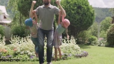 Sakallı ve Kardeşleri Kollarında İki Okul Öncesi Çocuğu Asılı Mutlu Aile Babası. Baba, Kız ve Oğul, Güneşli Yaz Günü 'nde Idyllic Banliyö Evinin arka bahçesinde eğlenceli oyunlar oynuyor..