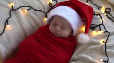Yeni doğan bebeğin ilk portresi beyaz çelenk arka planında kırmızı beze sarılı, Noel Baba şapkalı komik uyuyan bebek. Mutlu Noeller, Mutlu yıllar, Bebek, Çocukluk, Kış Konsepti