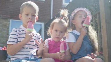 Three cute little Children enjoys delicious ice cream cone. Child eating watermelon popsicle. Kids Siblings snack sweets in Home Garden. Summer holiday Hot weather Sunny Day. Childhood, Food Candy.
