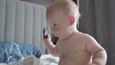 Yakın plan mutlu, uykucu çocuk 10 aylık. Yeni doğan çocuk, beyaz yumuşak yatakta banyo sonrası kameraya bakıyor. Bebek yatmadan önce esner. Çocukluk, annelik, aile, bebek konsepti.