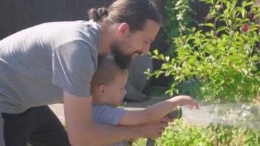 Baba ve Oğul. Bahçenin arka bahçesinde babamla birlikte çimenleri sulayan komik küçük çocuk. Yazlık iş. Açık havada çalışkan bir anaokulu çocuğu. Çocuklar ev işlerine yardım eder. çocuklar için etkinlik.