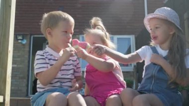 Three cute little Children enjoys delicious ice cream cone. Child eating watermelon popsicle. Kids Siblings snack sweets in Home Garden. Summer holiday Hot weather Sunny Day. Childhood, Food Candy.