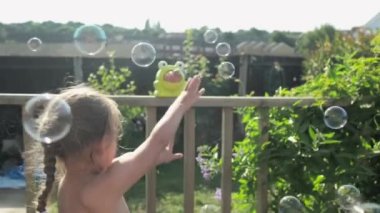 Hot Sunny Day outside the garden. blowing and catch spray bubbles with Hands. Happy Funny Kids enjoy playing catching Bubbles. Holidays in the countryside, summer holidays leisure. Real life Childhood