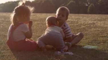 people in the park. happy family silhouette sitting on grass at sunset. mom with three kids eating fruits Grapes snack picnic time. children playing spend time outside. parents Friendship Siblings.