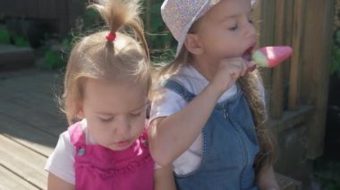 Two Sisters Children enjoys delicious ice cream cone. Child eating watermelon popsicle. Kids Siblings snack sweets in Home Garden. Summer holiday Hot weather Sunny Day. Childhood, Food Candy Friends.