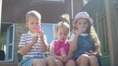Three cute little Children enjoys delicious ice cream cone. Child eating watermelon popsicle. Kids Siblings snack sweets in Home Garden. Summer holiday Hot weather Sunny Day. Childhood, Food Candy.