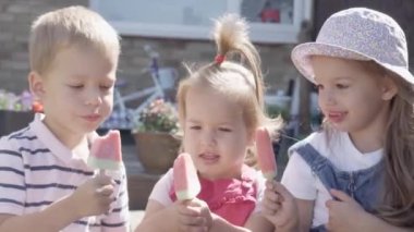 Three cute little Children enjoys delicious ice cream cone. Child eating watermelon popsicle. Kids Siblings snack sweets in Home Garden. Summer holiday Hot weather Sunny Day. Childhood, Food Candy.