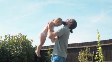 Mutlu aile baba ve bebek tatillerini bahçede ya da parkta geçiriyor. Babam kusar ve çocuğu yakalar. Gülümseyen ebeveynler birlikte vakit geçiriyorlar. Babacığın kucağında yeni yürümeye başlayan çocuğu.