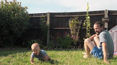Arka bahçedeki çimenlikte emekleyen bebek çocuk. Bahçe Yaz Saati 'nde bebek ve baba. Aile zamanı dışarıda bir araya geliyor. Sıcak Güneşli Gün. Çocukluk Gelişimi.