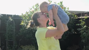 Happy family mother and baby enjoying the summer holidays in the garden or park. Mum throws up and catches the child. Smiling parents spending leisure time together.Mom holds toddler on arms.