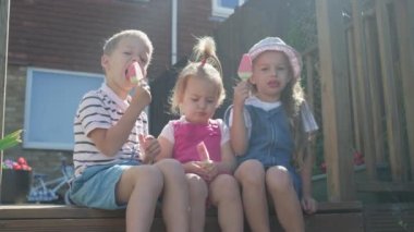 Three cute little Children enjoys delicious ice cream cone. Child eating watermelon popsicle. Kids Siblings snack sweets in Home Garden. Summer holiday Hot weather Sunny Day. Childhood, Food Candy.