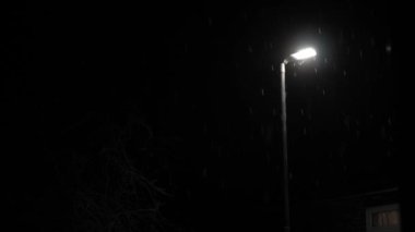 Birleşik Krallık 'taki ilk kar yağışı örtüsü kara arka planda. Gece Yolu 'ndaki Lambanın Işığında Düşen Kar Taneleri Kış, Yavaşça Düşen Kar Etkisi. Hava Durumu, Anomali, Acil Durum Konsepti.