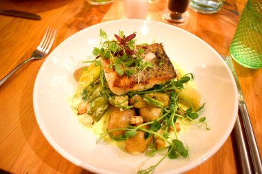 Mevsimlik market balığı, kereviz, haşlanmış pırasa, bebek yeni patatesler, ahşap masadaki beyaz tabakta dereotu ve beyaz şarap sosu..