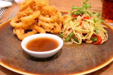 Tay baharatlı Papaya salatası ve tatlı sosuyla servis edilen Çıtır Kalamar halkalarını yakın plan..