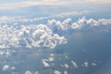 Deniz suyunun üzerinde süzülen beyaz bulutlar boyunca uçak penceresinin yüksek irtifasından görüldü..