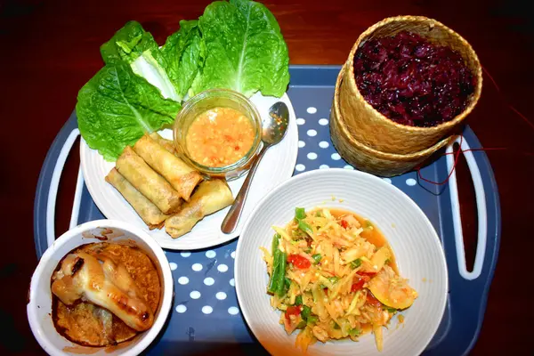 A set of Thai food with a dish of Spring rolls, Chicken roasted, Spicy mango salad side dish with black sticky rice. Easy cooking at home with Thai food.