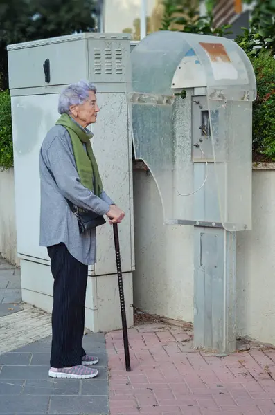 stock image The elderly woman stands like a monument beside the dismantled payphone, both relics of a forgotten era.