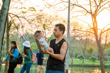 Baba, şehir parkında gün batımı eğlencesi için bebeği kucağına aldı.