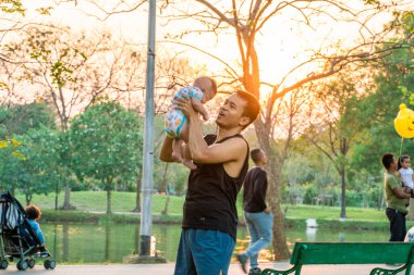 Baba, şehir parkında gün batımı eğlencesi için bebeği kucağına aldı.