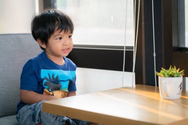 Sevimli küçük çocuk rahat bir kanepede sabah güneşiyle oturuyor.