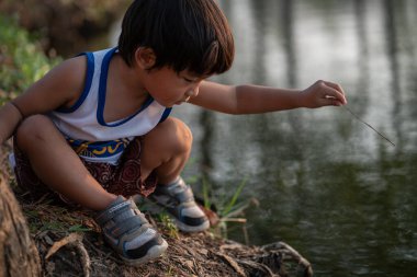 Asian boy sitting under tree sunset time lookimg to the river summer recreation outdoor activity