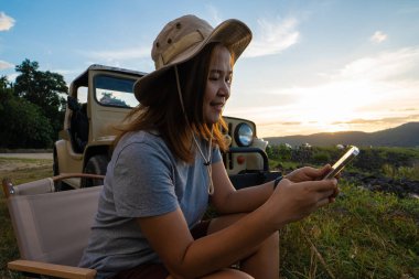 Asyalı kadın yaz tatili konseptiyle kamp yaparken akıllı telefon kullanıyor.