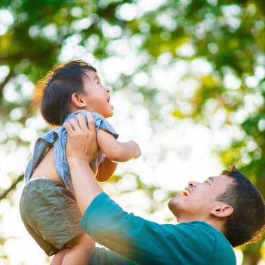 Mutlu bir babanın portresi, küçük oğlunun elini tutuyor. Şehir parkında gün batımında taşınıyor. Babasıyla dışarıda oynayan tatlı çocuk..