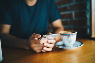 Business man hand use smartphone drinking hot coffee sitting in cafe hand close up