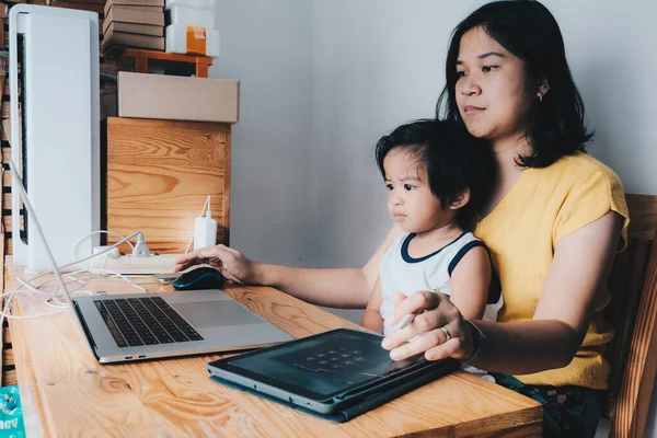 Young asian mother working with laptop work from home sitting with baby boy in living room