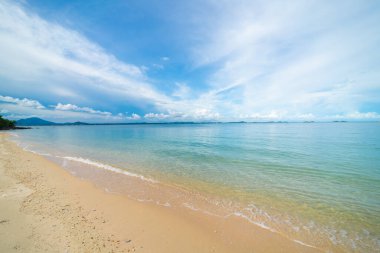 Deniz sahili dalgaları beyaz kumsalda mavi gökyüzü bulutlarına karşı yaz tatili